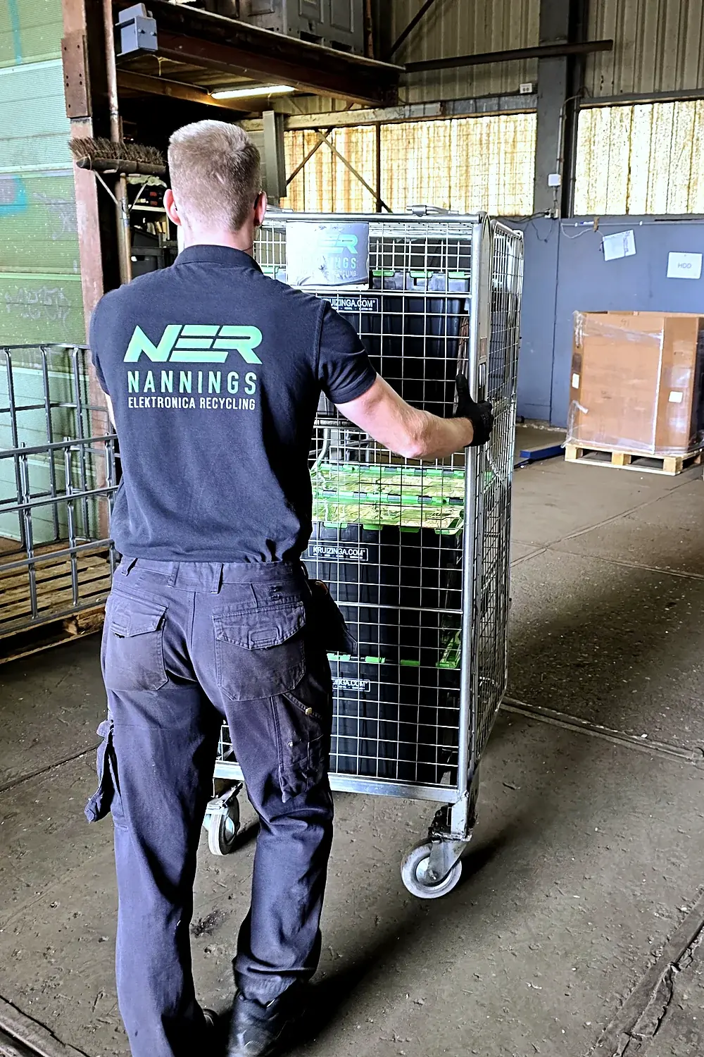 Medewerker van Nannings Elektronica Recycling duwt een volle rolcontainer met ingezamelde apparatuur naar de bakwagen